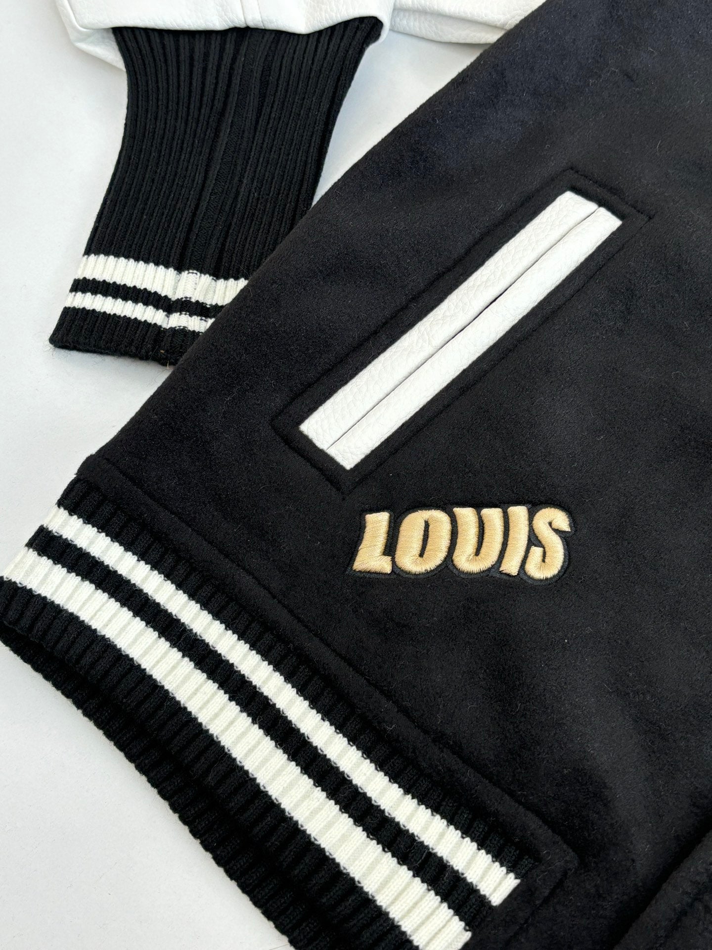 Louis Vuitton varsity jacket sleeve cuff close-up with ribbed stripes and gold “LOUIS” lettering
