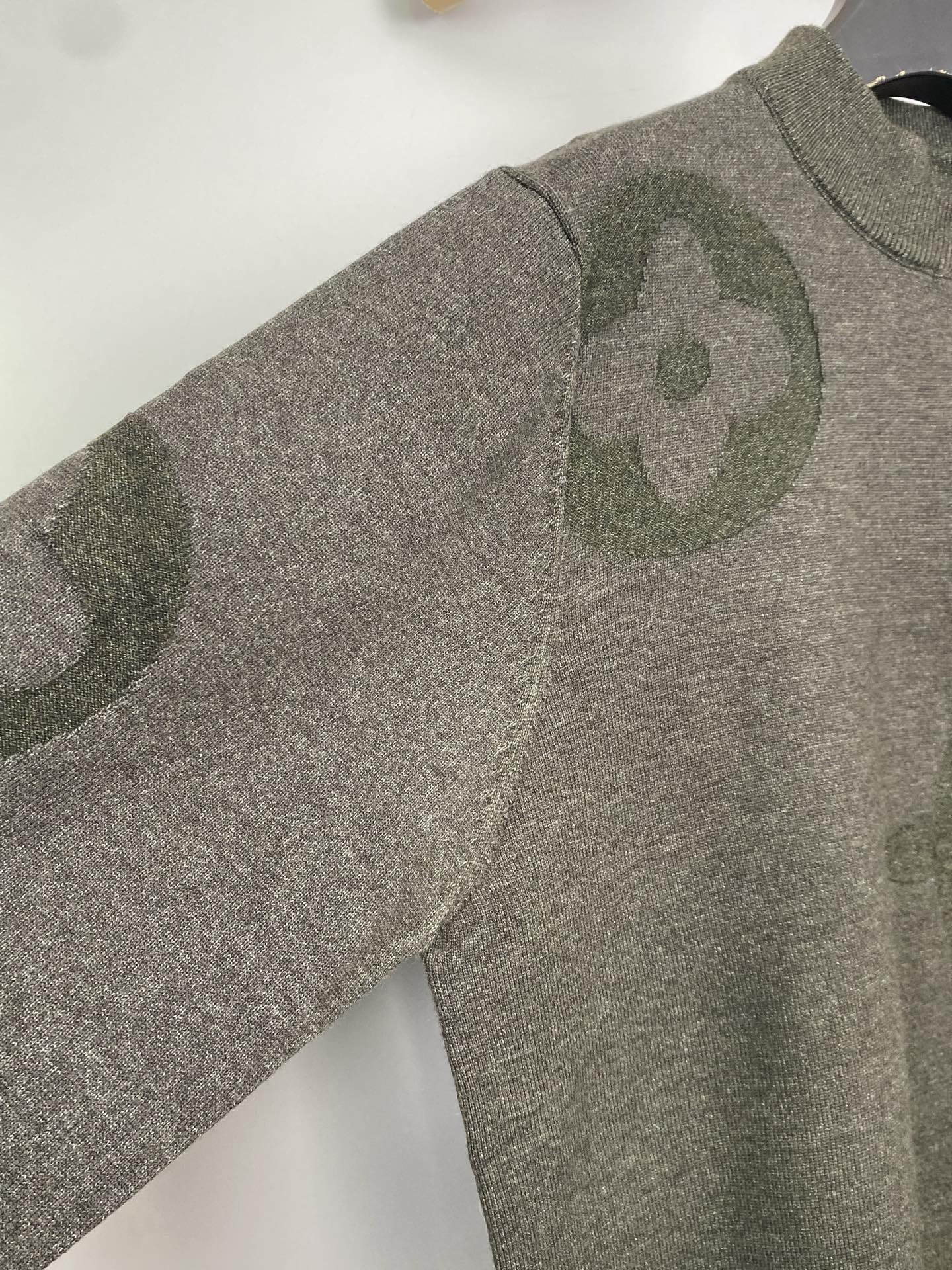 Grey knit sweater with allover logo pattern, long sleeves, angled view on hanger