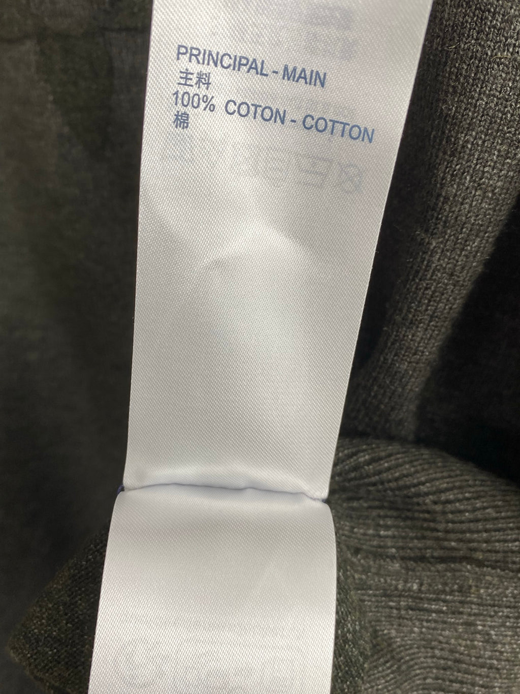 Clothing care label reading 100% coton, inside seam at grey knit sweater