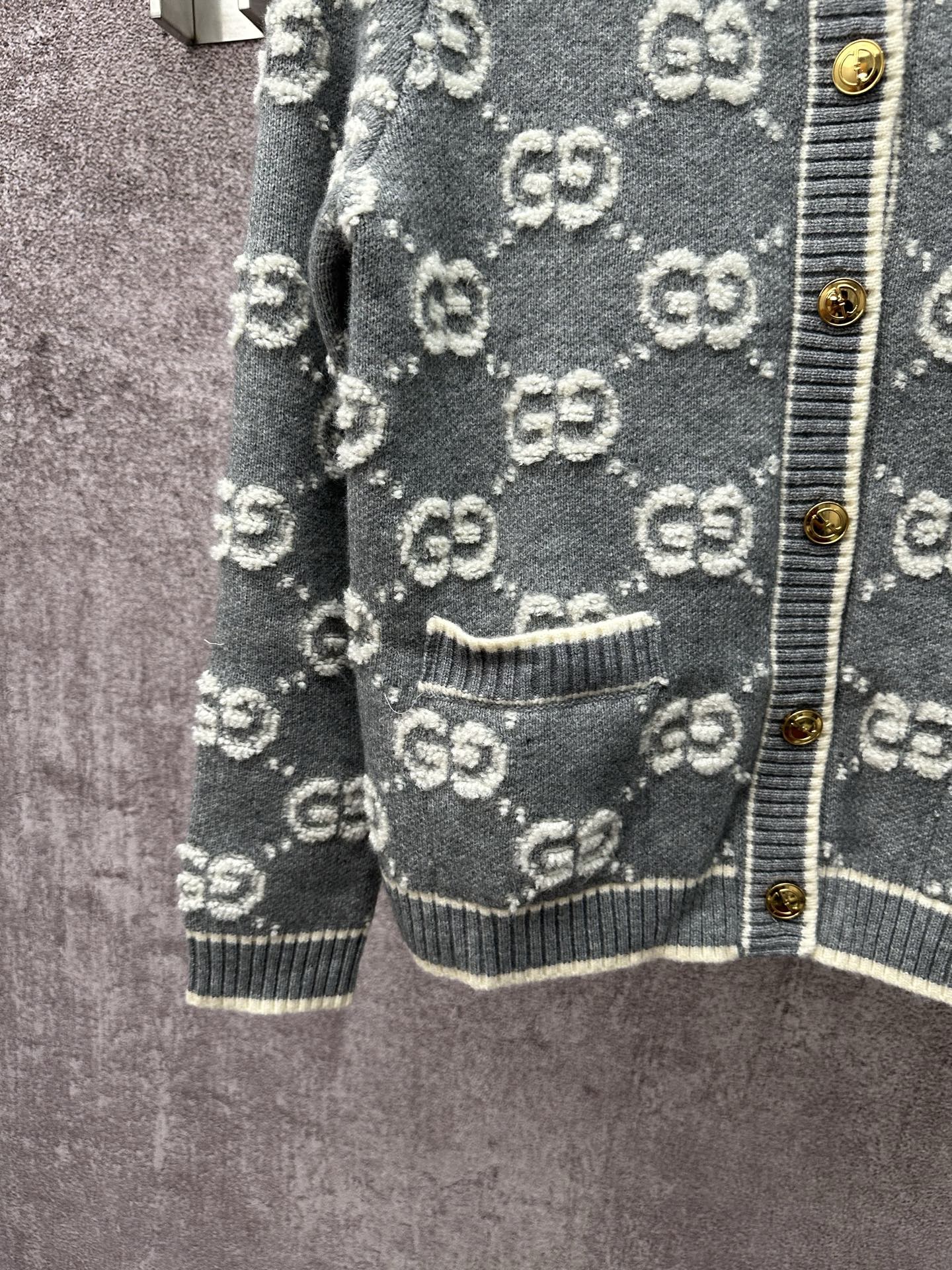 Gucci dark green cardigan with GG pattern, ribbed pocket trim, and gold button placket edge.