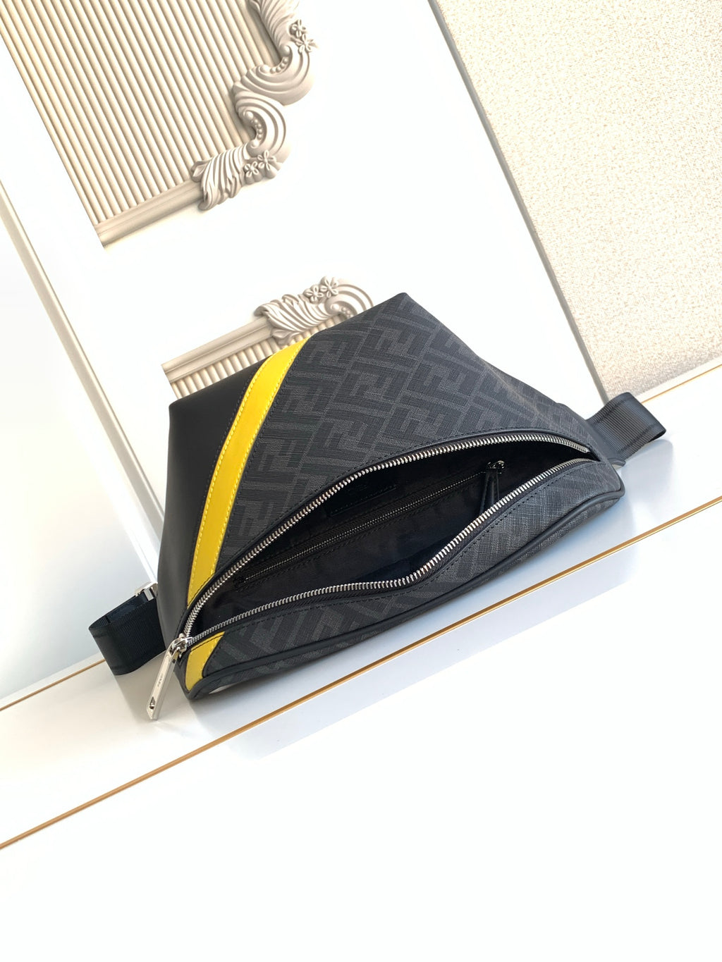 Fendi bag with dark logo-print exterior, neon yellow side stripe, and front zipper closure.