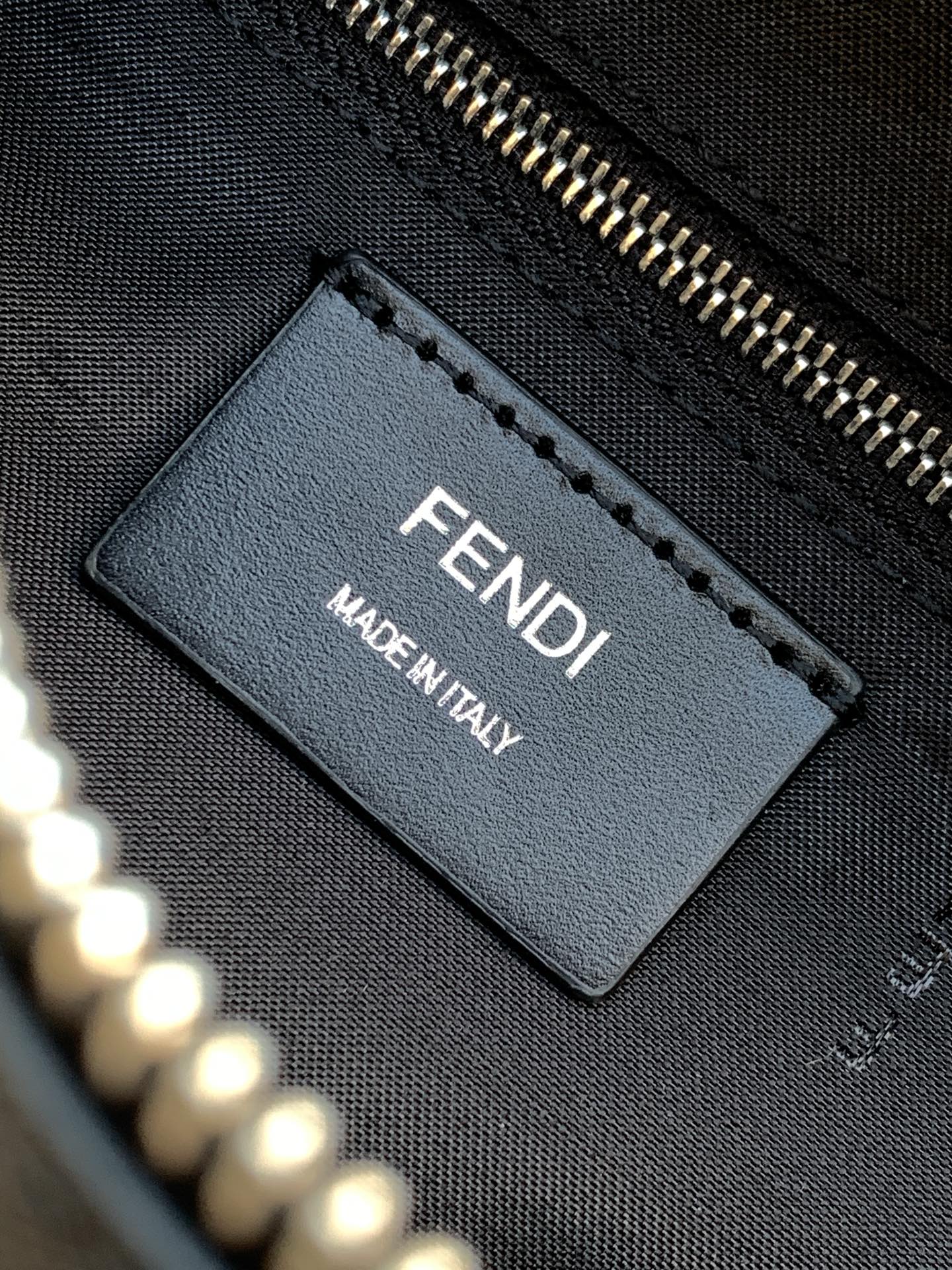 Fendi bag interior label tag reading FENDI and MADE IN ITALY on dark fabric.