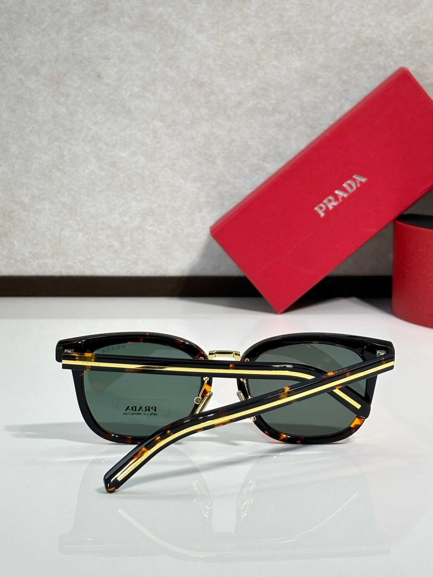 Dark sunglasses with gold-tone top bar and green-tinted lenses; rounded frames.