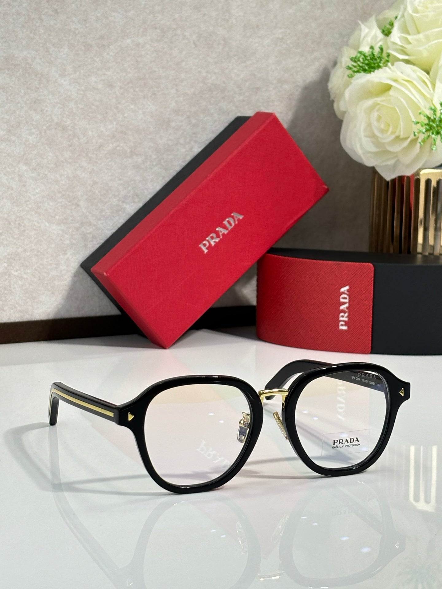 Prada eyeglasses with black round frames and clear lenses, gold accents on temples.