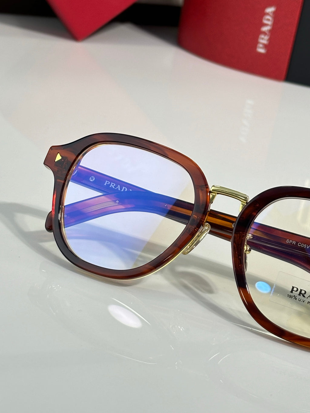 Prada eyeglasses with brown round frames and blue-tinted lens, logo on lens center.
