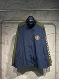 Blue and green long-sleeve windbreaker jacket with zip front and crest patch at chest