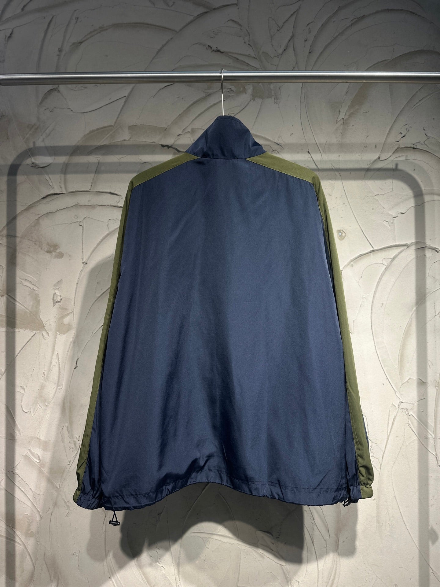 Blue windbreaker jacket back view with hood and contrasting green side panels