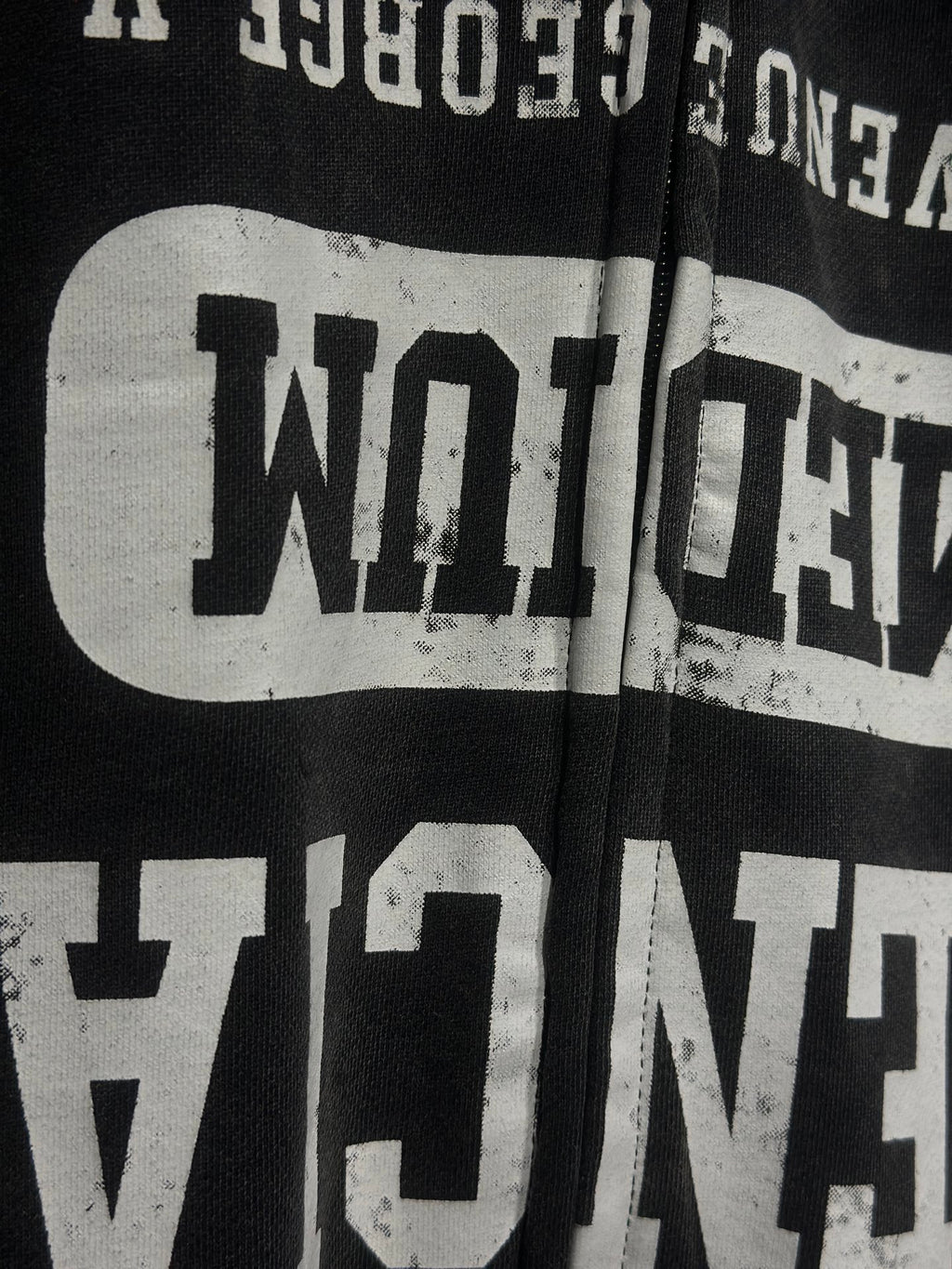 Close-up of black hoodie chest graphic with distressed white text and zipper edge