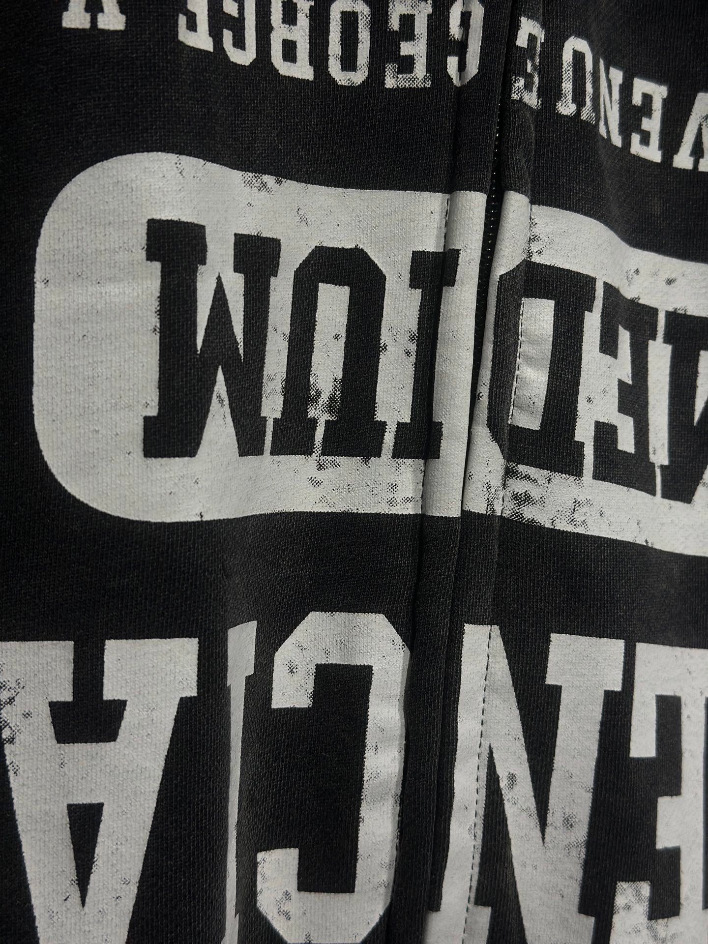 Close-up of black hoodie chest graphic with distressed white text and zipper edge
