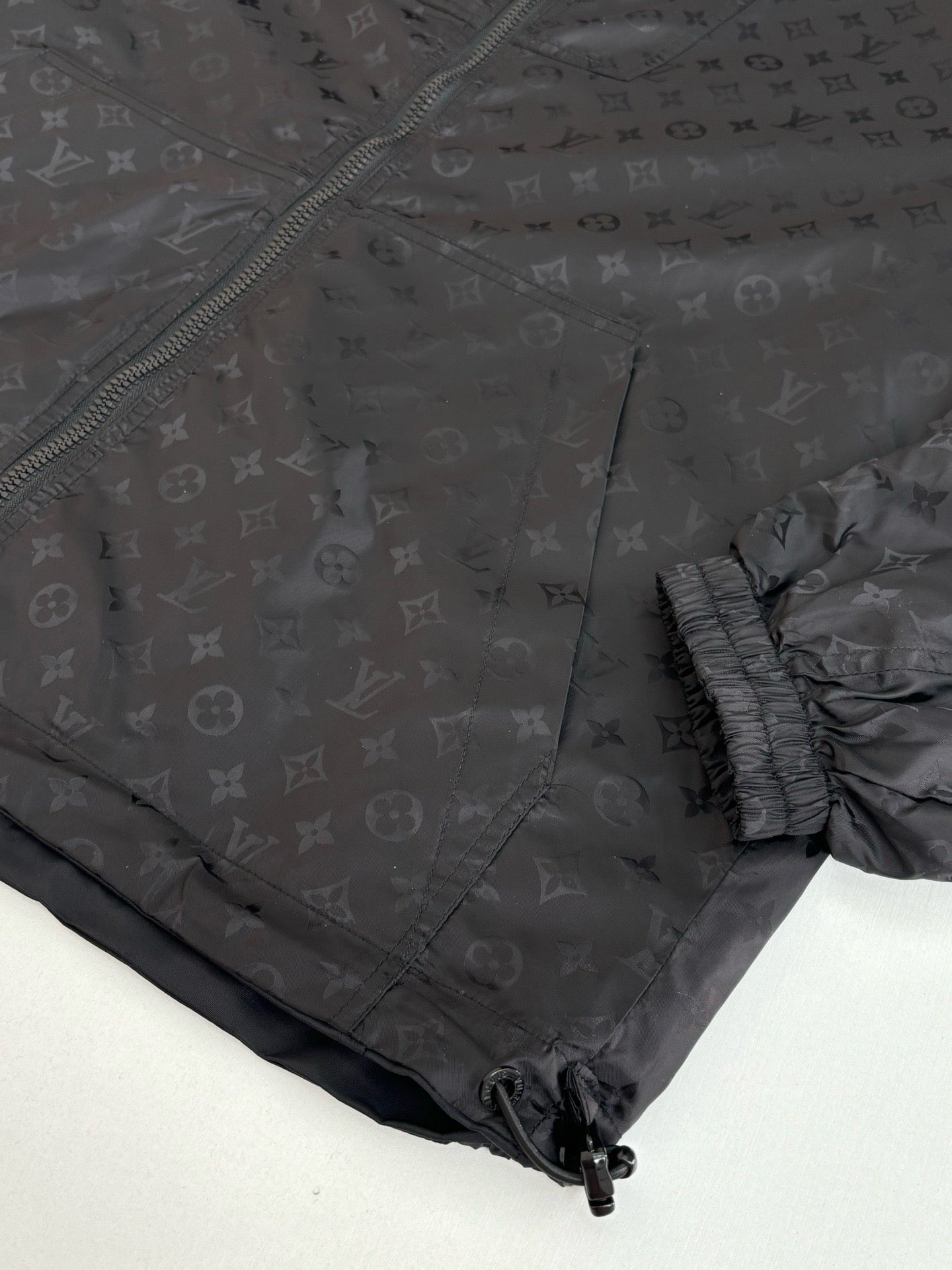 Dark navy hooded jacket with textured monogram pattern and elastic hem, side close-up