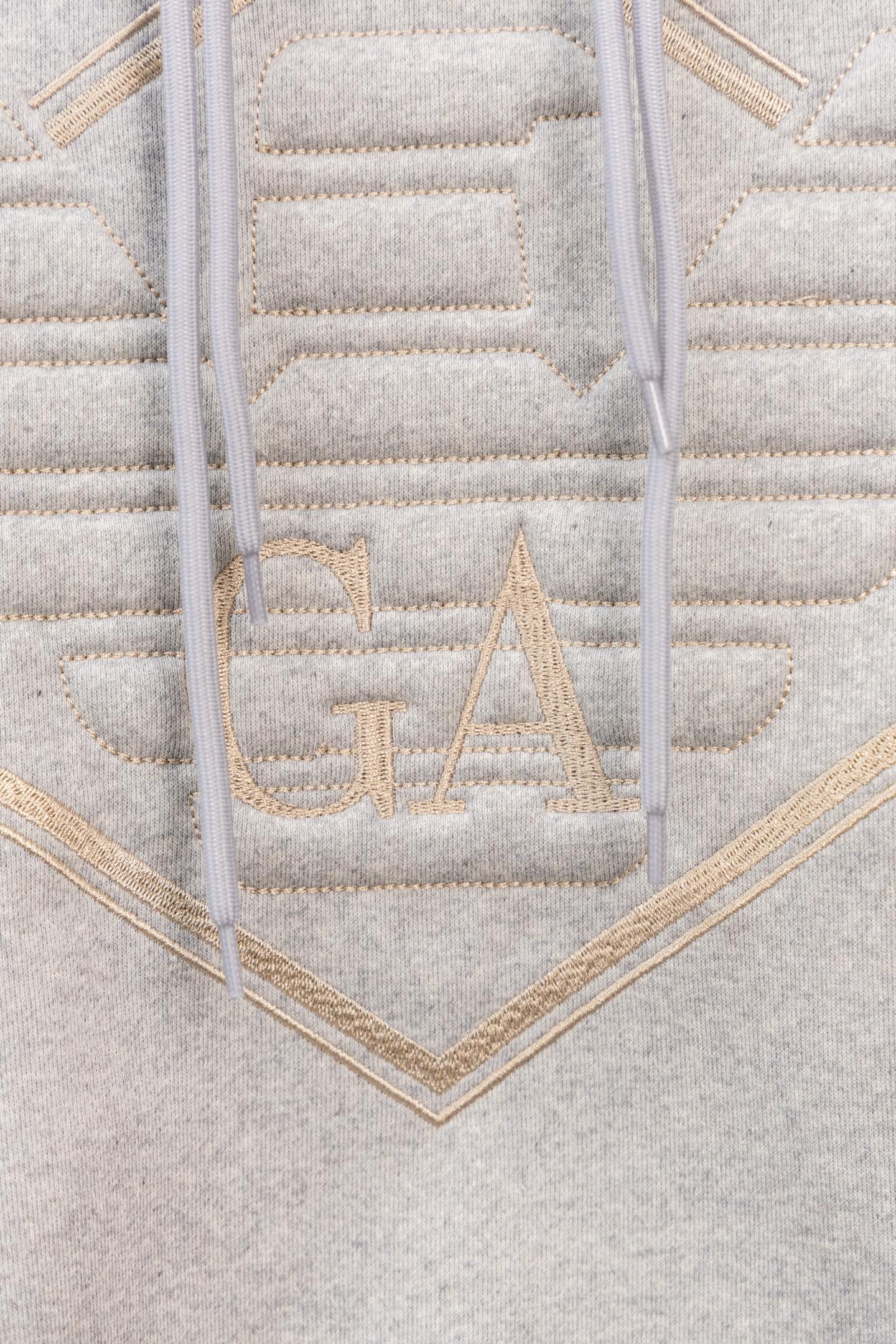 Amiri hoodie close-up of embroidered V logo with gold-toned stitched lettering