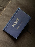 Fendi leather brand tag on brown fabric bag, stitched edges, printed logo.