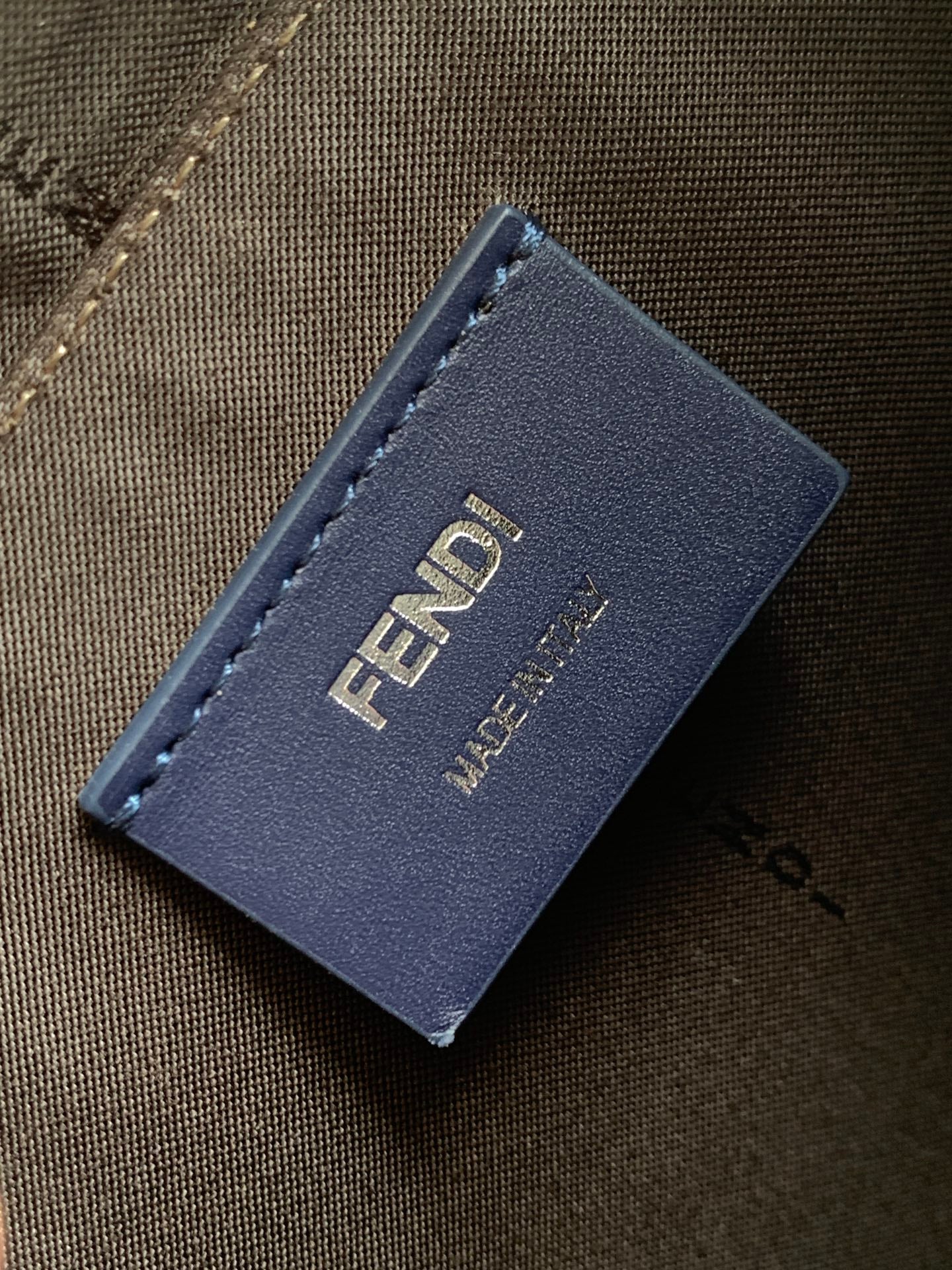 Fendi leather brand tag on brown fabric bag, stitched edges, printed logo.