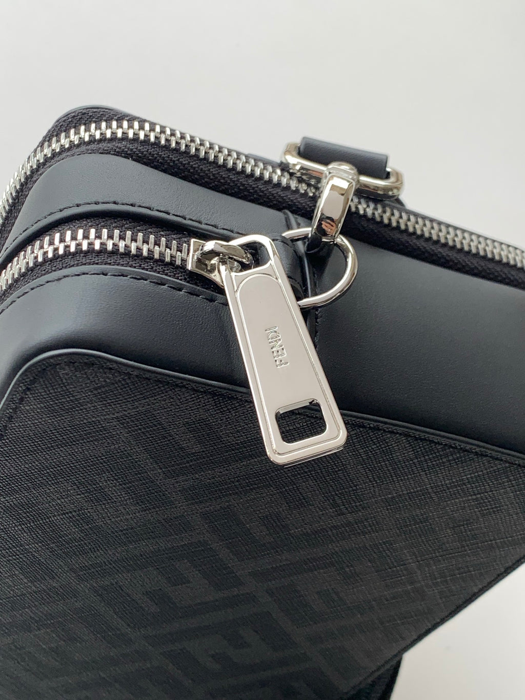 Black crossbody bag with silver hardware, zip pull, and keyring tab