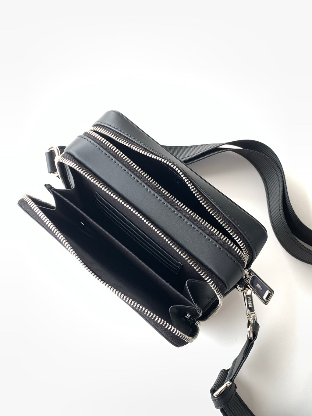 Black zip crossbody bag laid flat with detachable shoulder strap