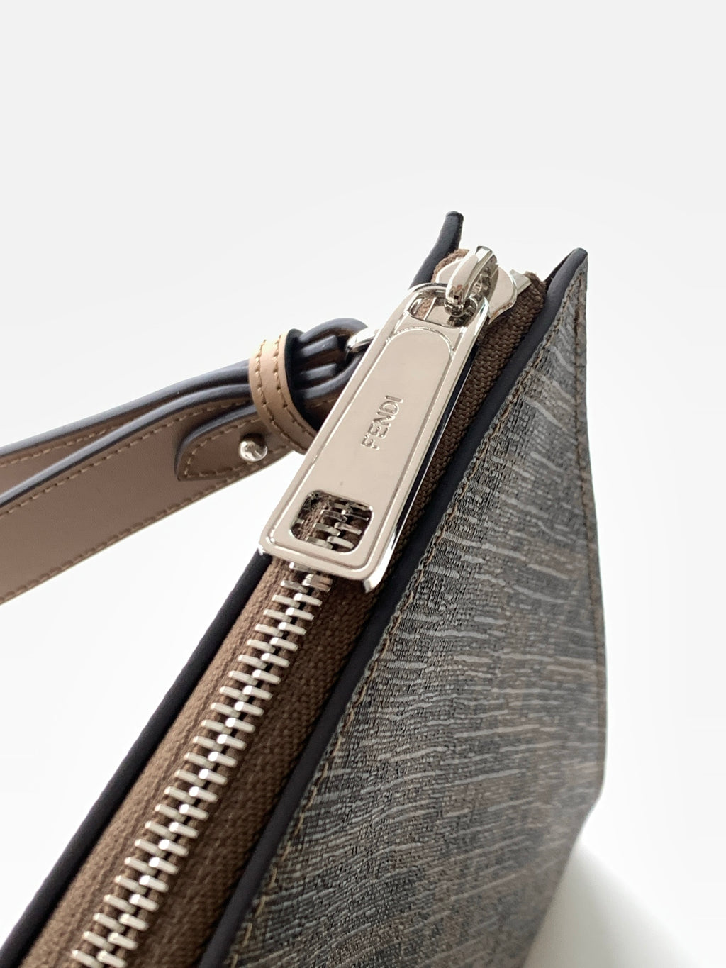Fendi logo clutch bag close-up of zipper track and tan handle attachment