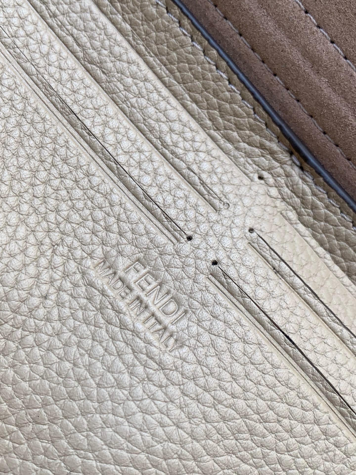 Fendi logo embossed on textured light-beige leather with dark edge trim