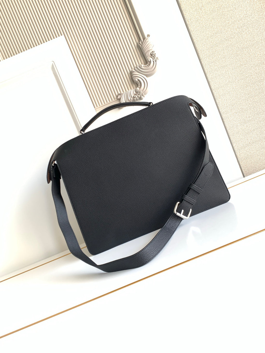 Black crossbody bag with flap closure and wide shoulder strap.