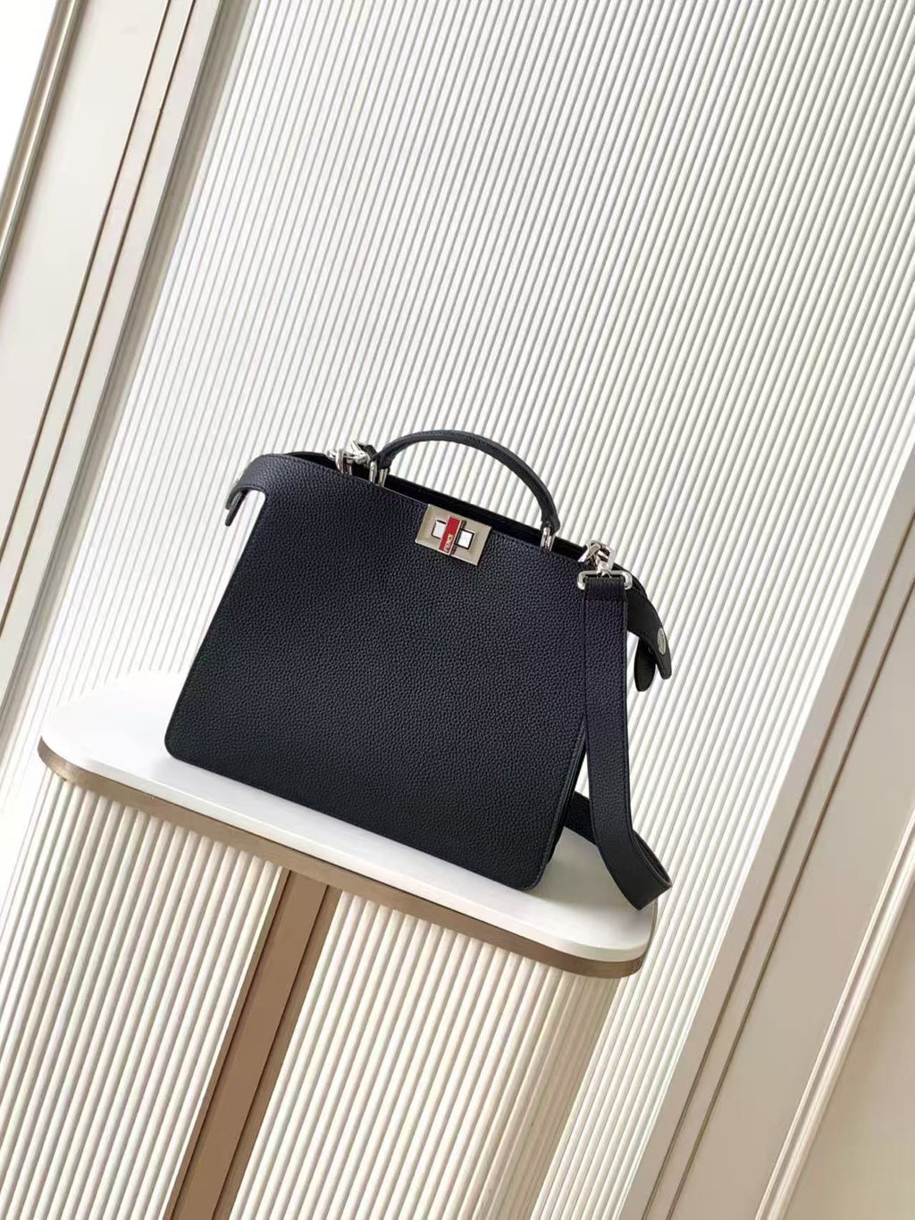 Black leather Fendi handbag with top handle and crossbody strap, front logo plaque