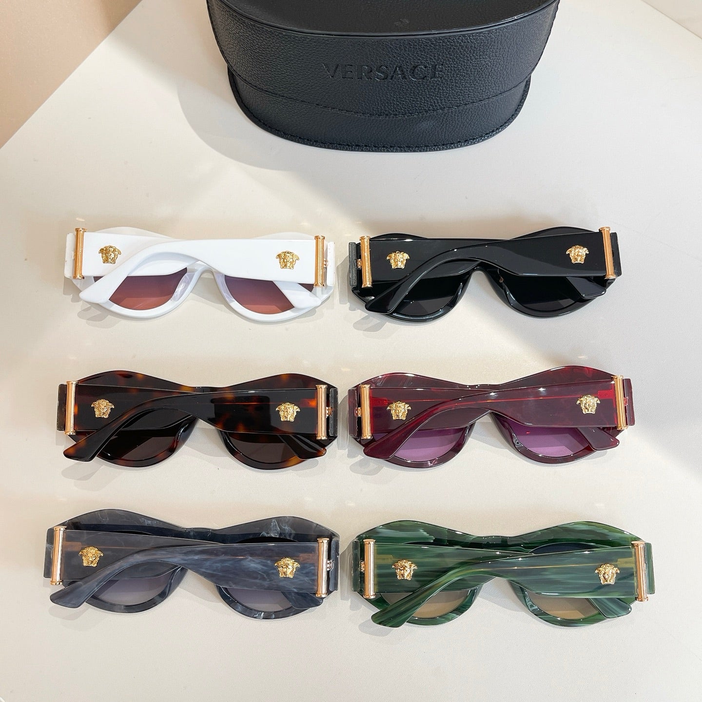 Versace sunglasses set with gold emblems in multiple colors, beside black case
