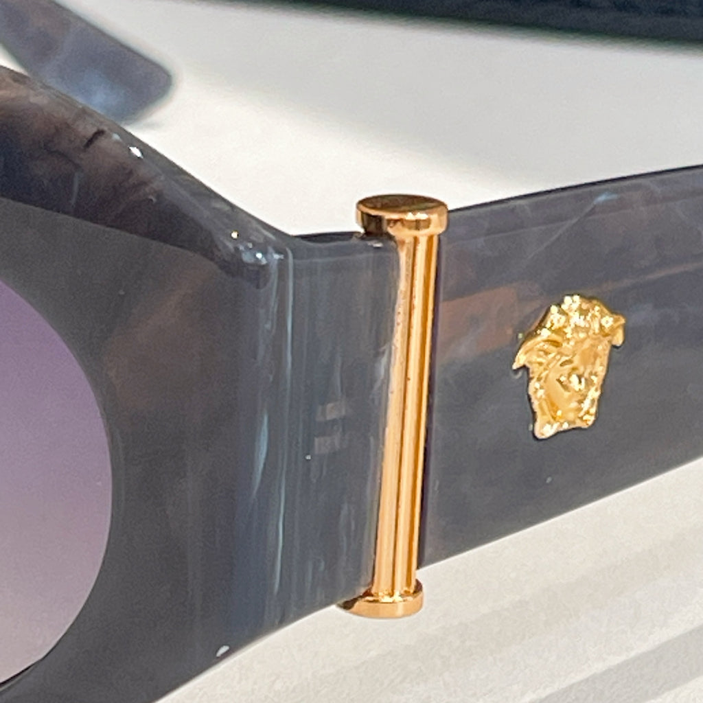 Sunglasses hinge close-up with gold vertical bar and Medusa-style emblem