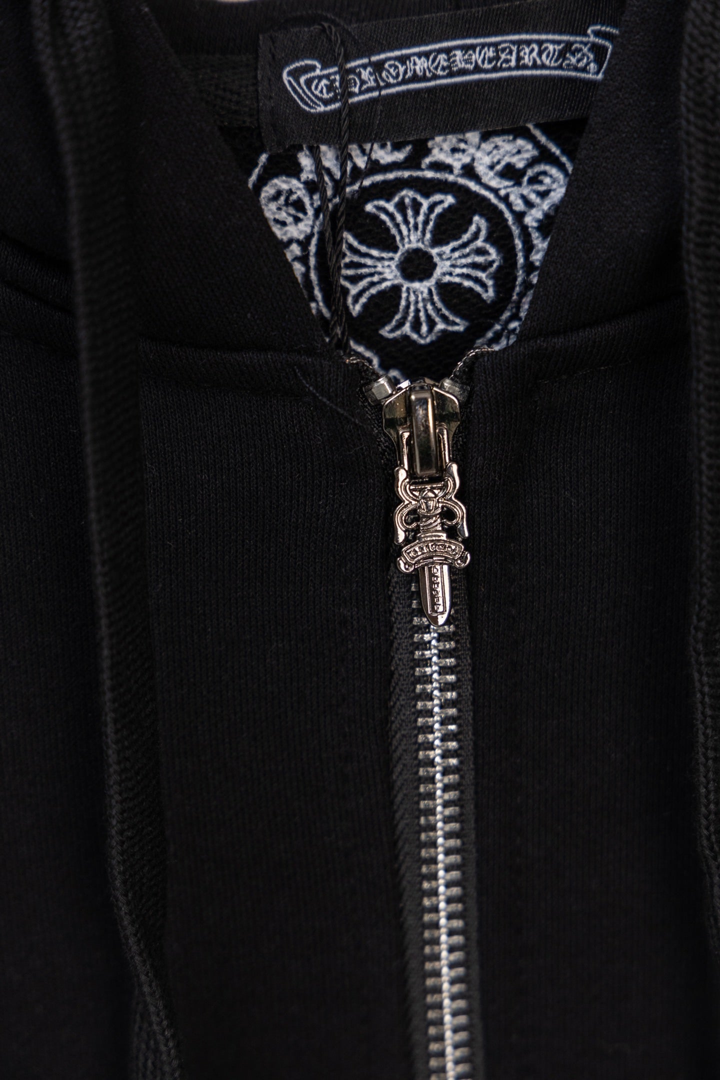 Black hoodie zipper and decorative emblem near the center placket