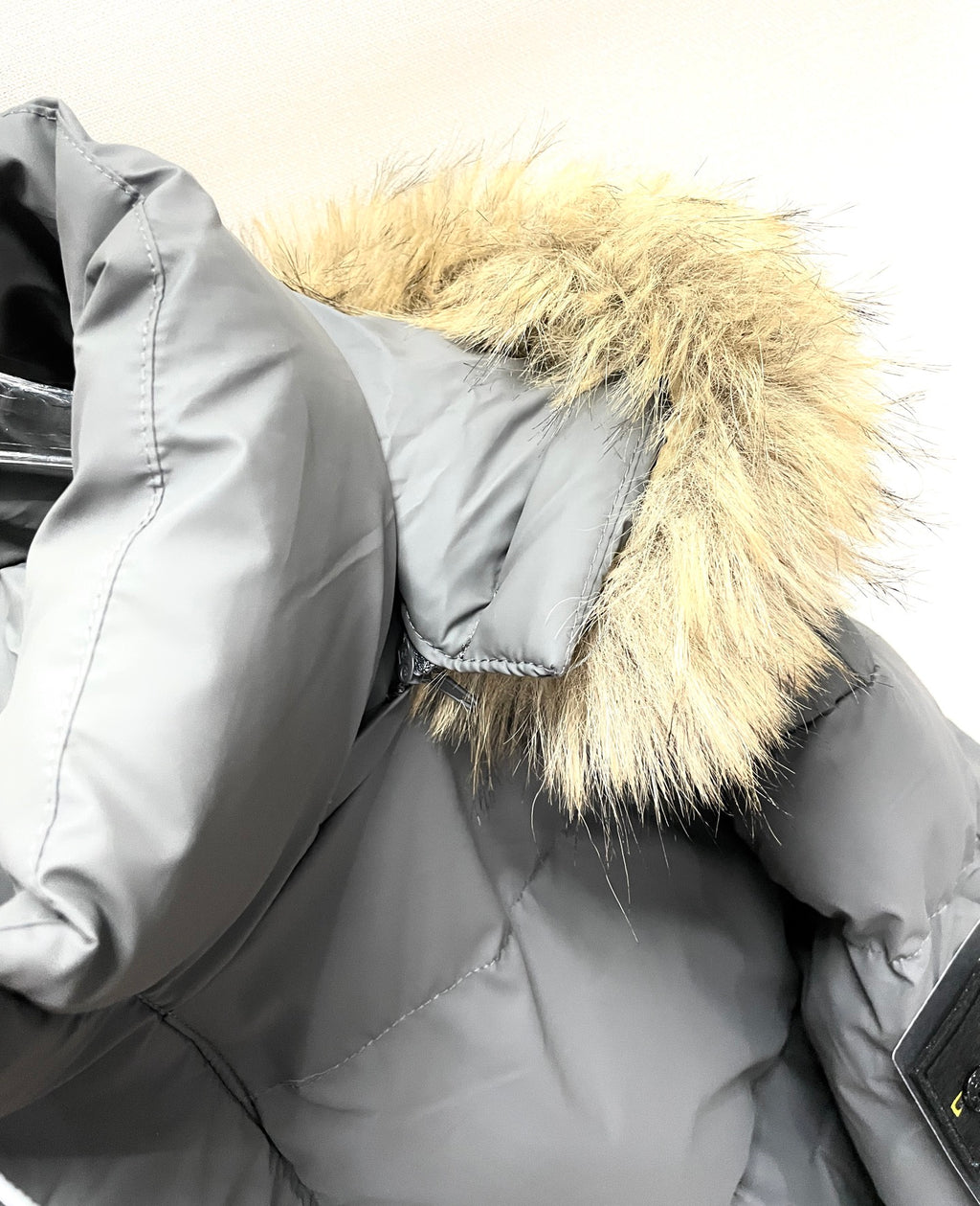 Gray puffer jacket close-up with faux fur hood trim and quilted stitching
