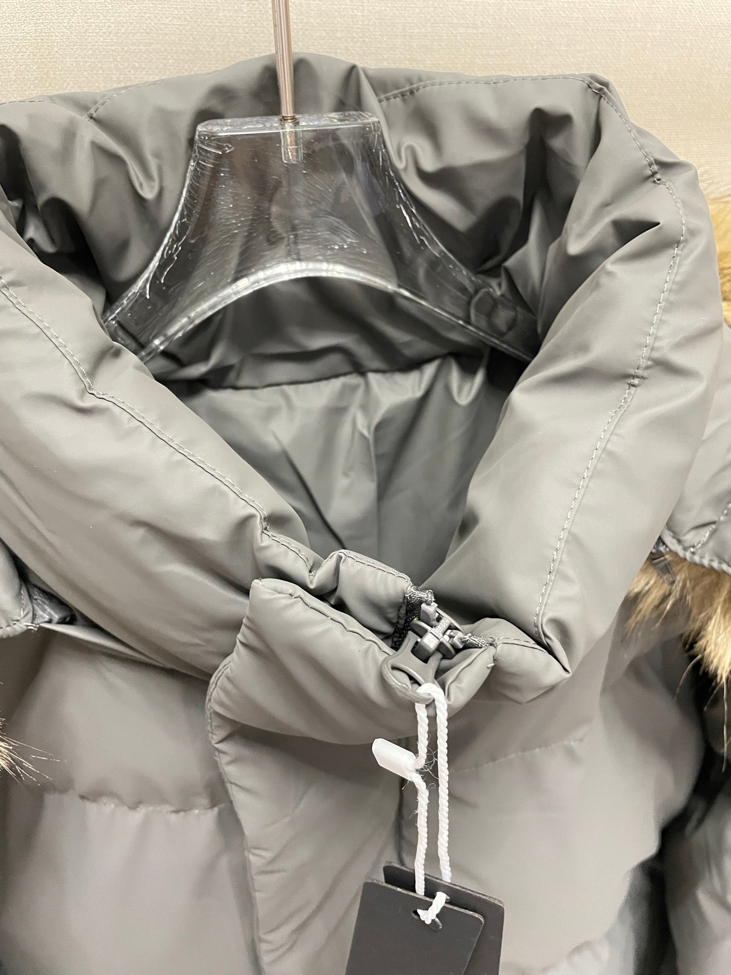 Gray puffer jacket interior close-up with drawcord hood and hanging size tag
