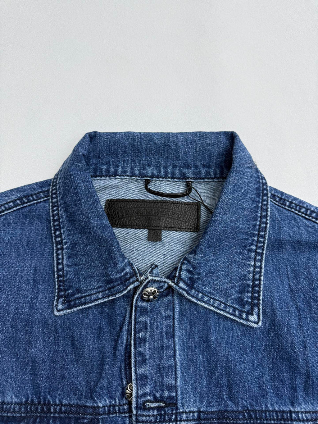 Denim jacket collar with dark logo patch and buttoned placket