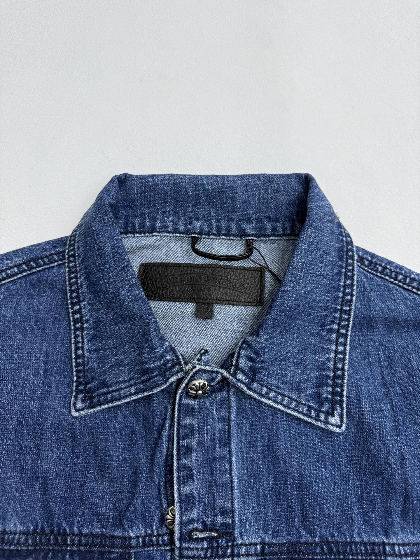 Denim jacket collar with dark logo patch and buttoned placket