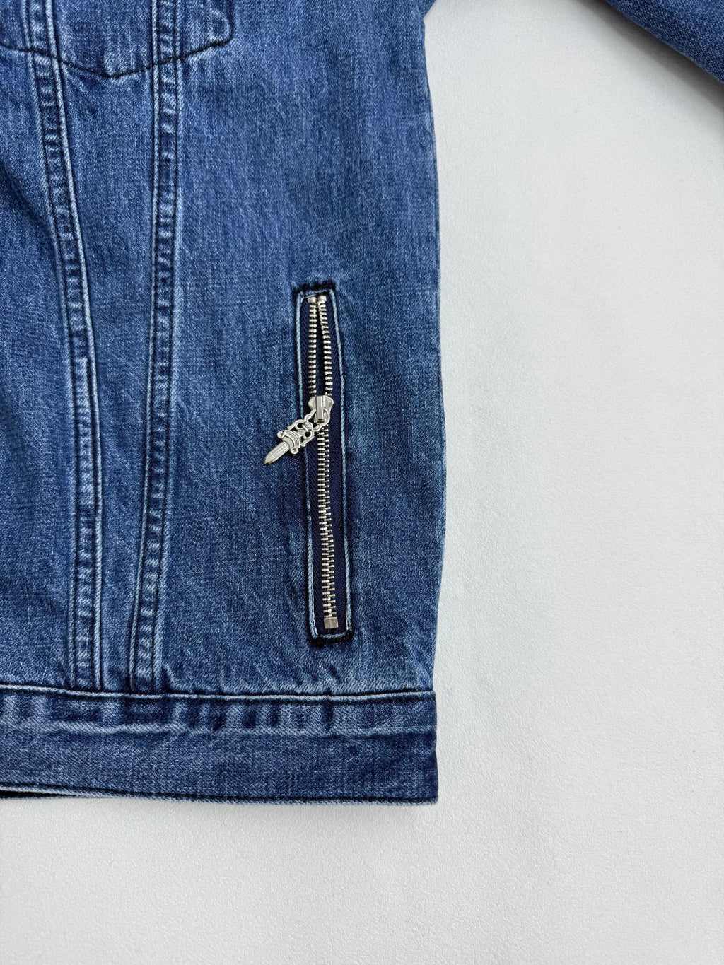 Blue denim jacket sleeve panel with vertical zipper pocket and metal pulls