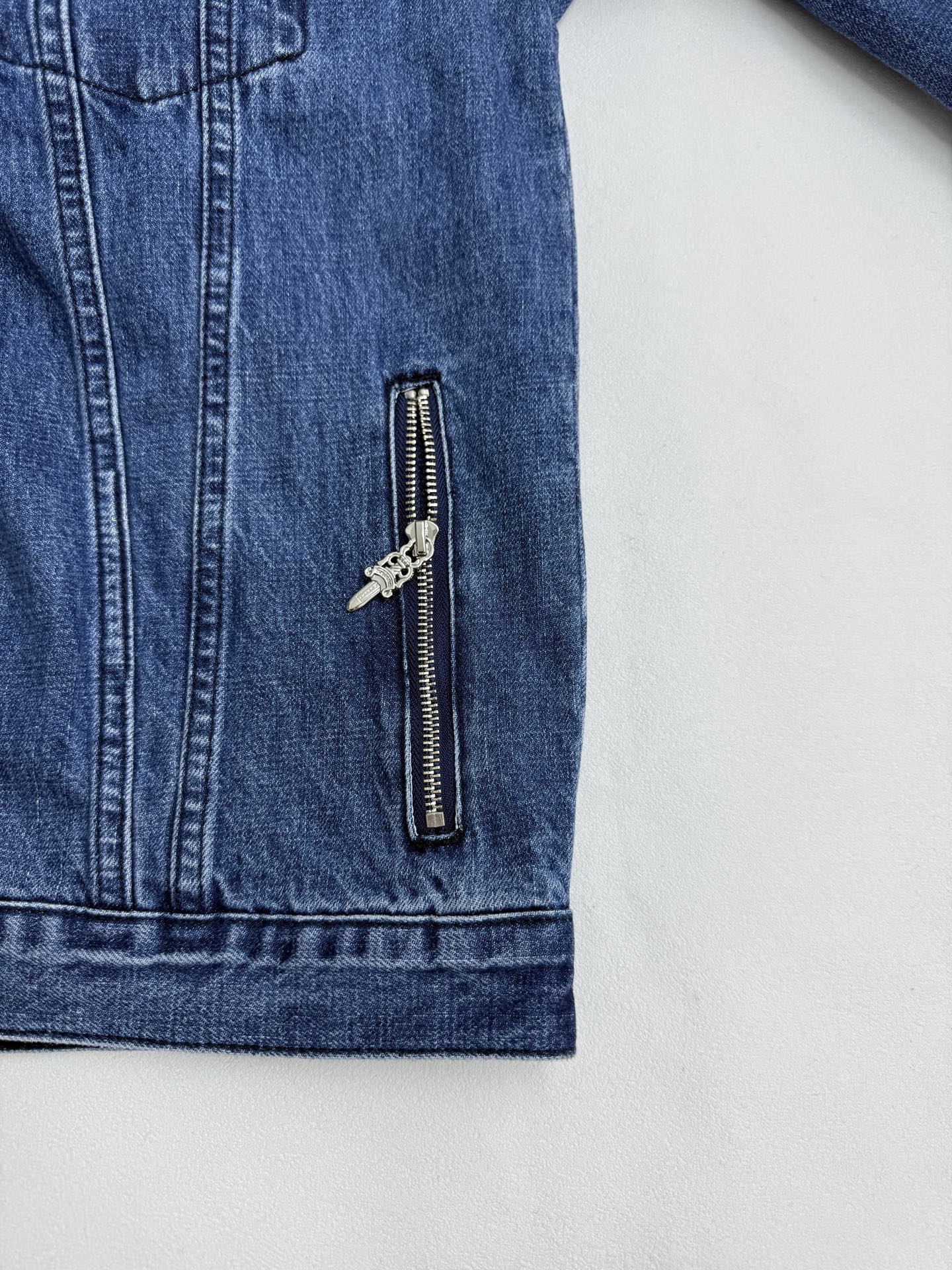 Blue denim jacket sleeve panel with vertical zipper pocket and metal pulls