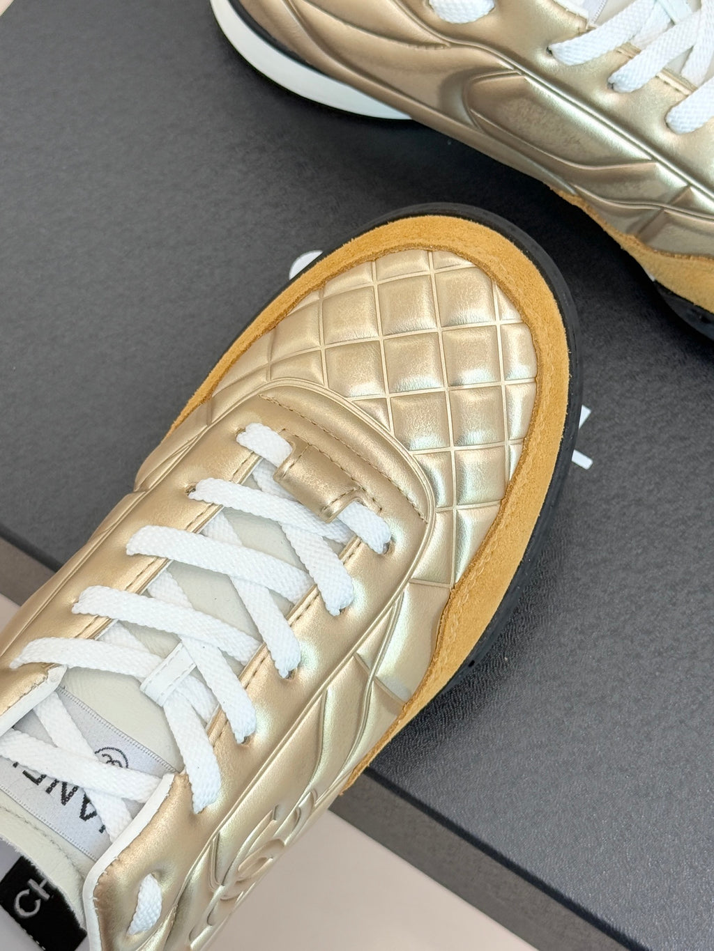 Chanel low-top sneaker close-up: gold quilted leather with white laces