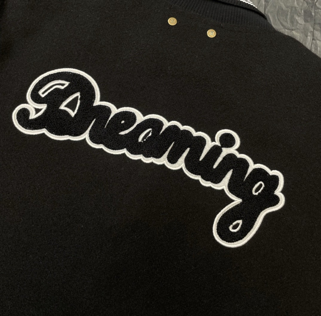 Louis Vuitton long varsity jacket embroidery close-up, white script “Dreaming” on black