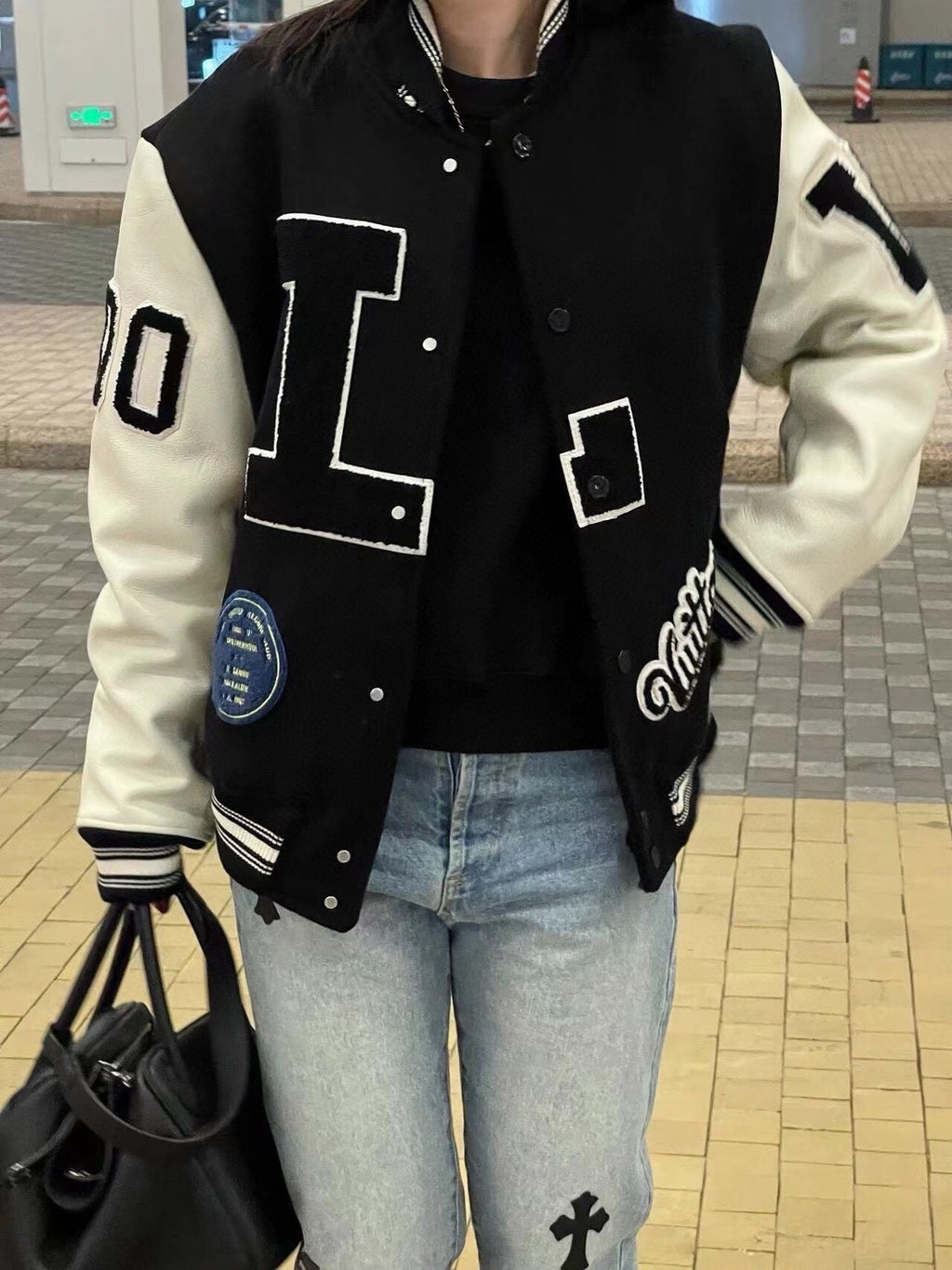 Louis Vuitton long varsity jacket worn with light blue jeans, black and white button front
