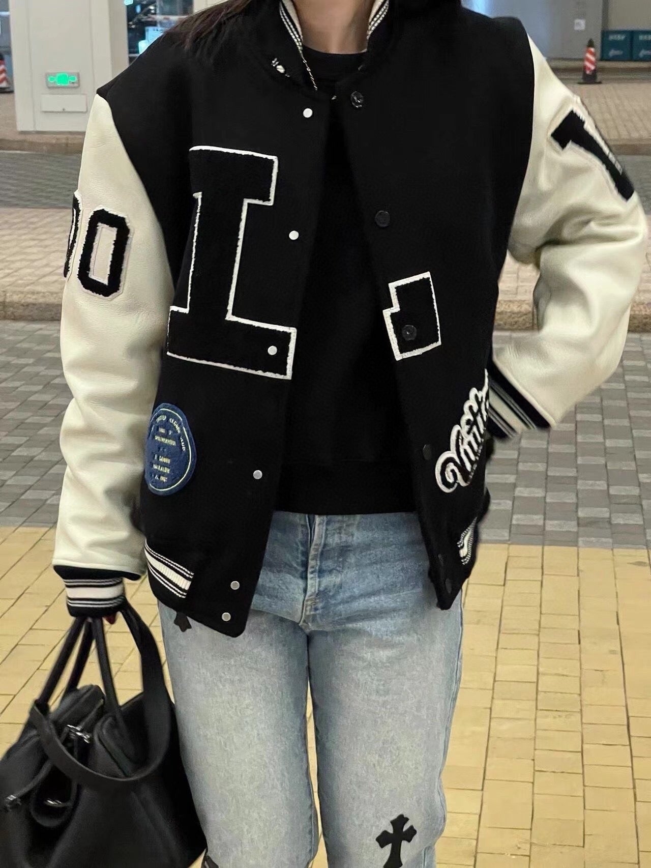 Louis Vuitton long varsity jacket worn with light blue jeans, black and white button front