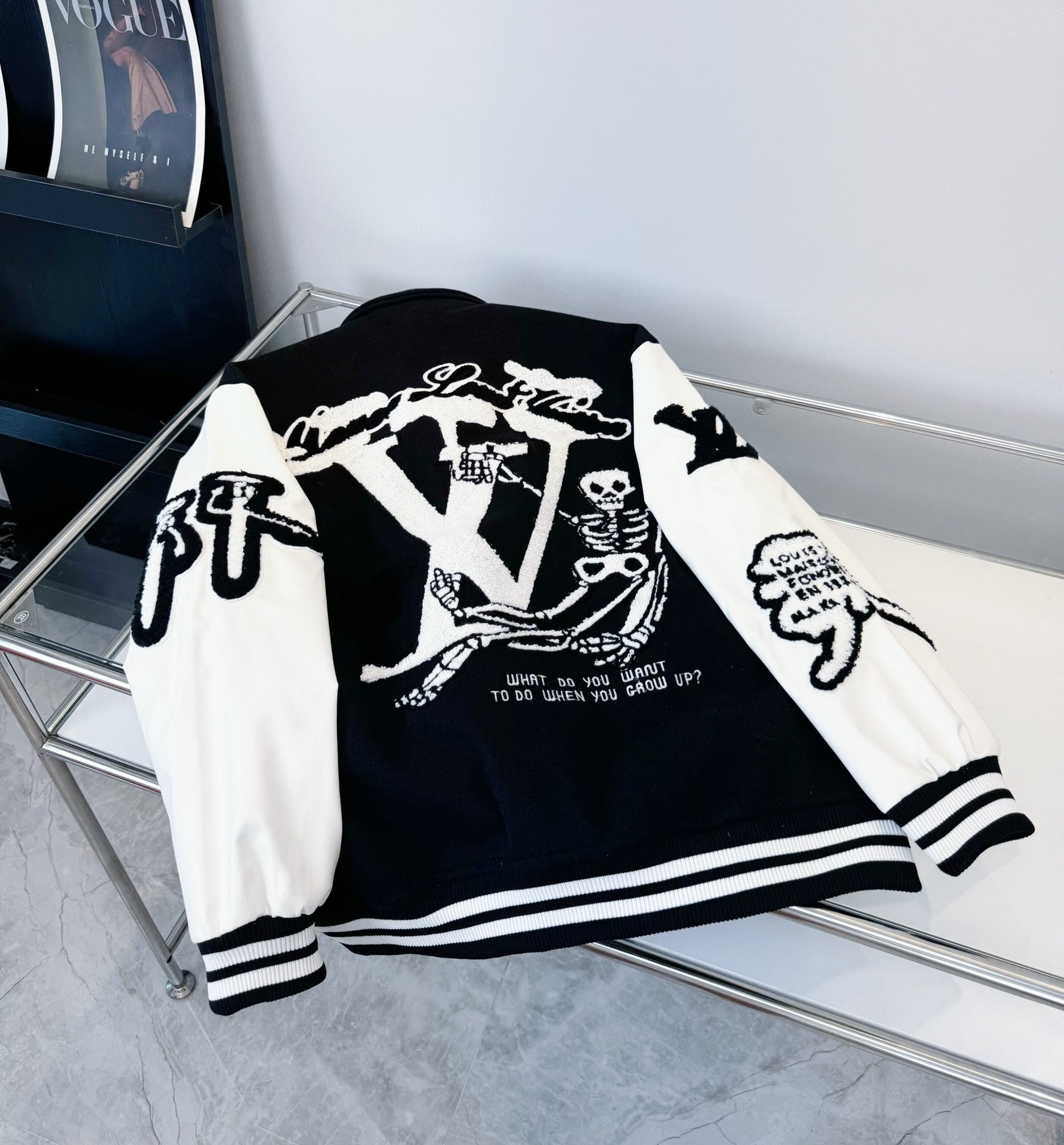 Black and white varsity-style jacket laid out, showing back graphic and striped cuffs