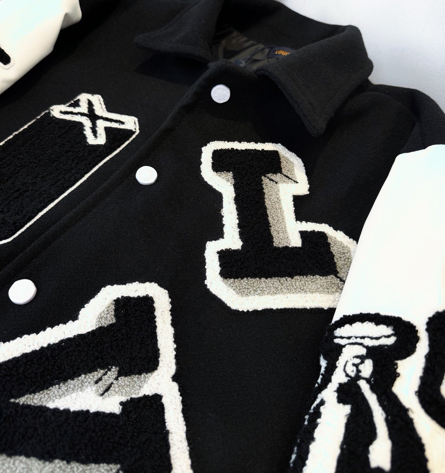 Close-up of black and white varsity-style jacket front with snap buttons and large letter graphic