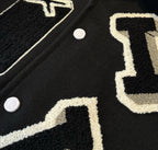 Close-up of black jacket fabric with bold white embroidered number and snap buttons