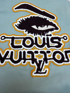 Light blue long-sleeve top with large black graphic text patch outlined in yellow