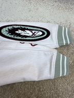 White long-sleeve top with oval graphic patch and green-striped ribbed cuff