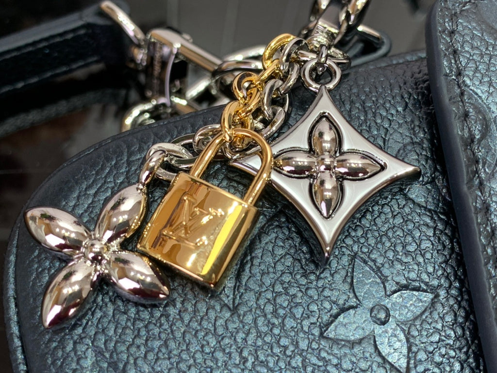 Gold and silver charm hardware on chain attached to dark teal embossed bag