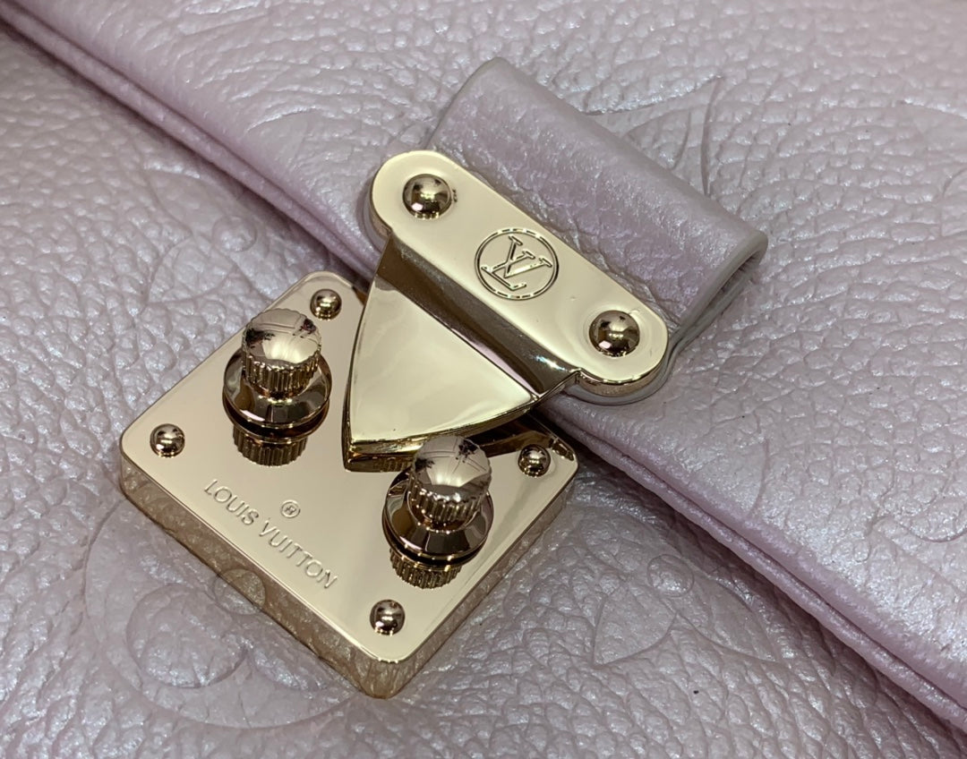 Gold turn-lock hardware on light pink textured leather handbag, close-up.