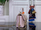 Light pink textured handbag with gold chain handles and orange top edge tab detail.
