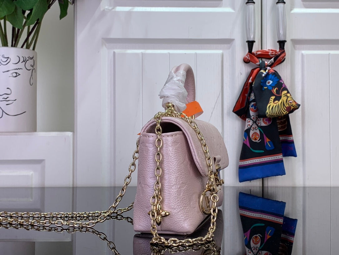 Light pink textured handbag with gold chain handles and orange top edge tab detail.