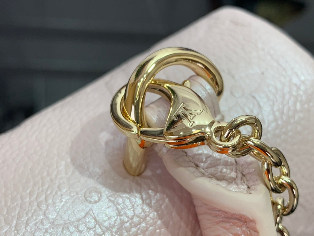 Gold D-ring and chain on light pink textured handbag, close-up on hardware.