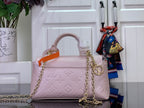 Light pink textured handbag with orange handle, gold chain strap, and gold ring detail.