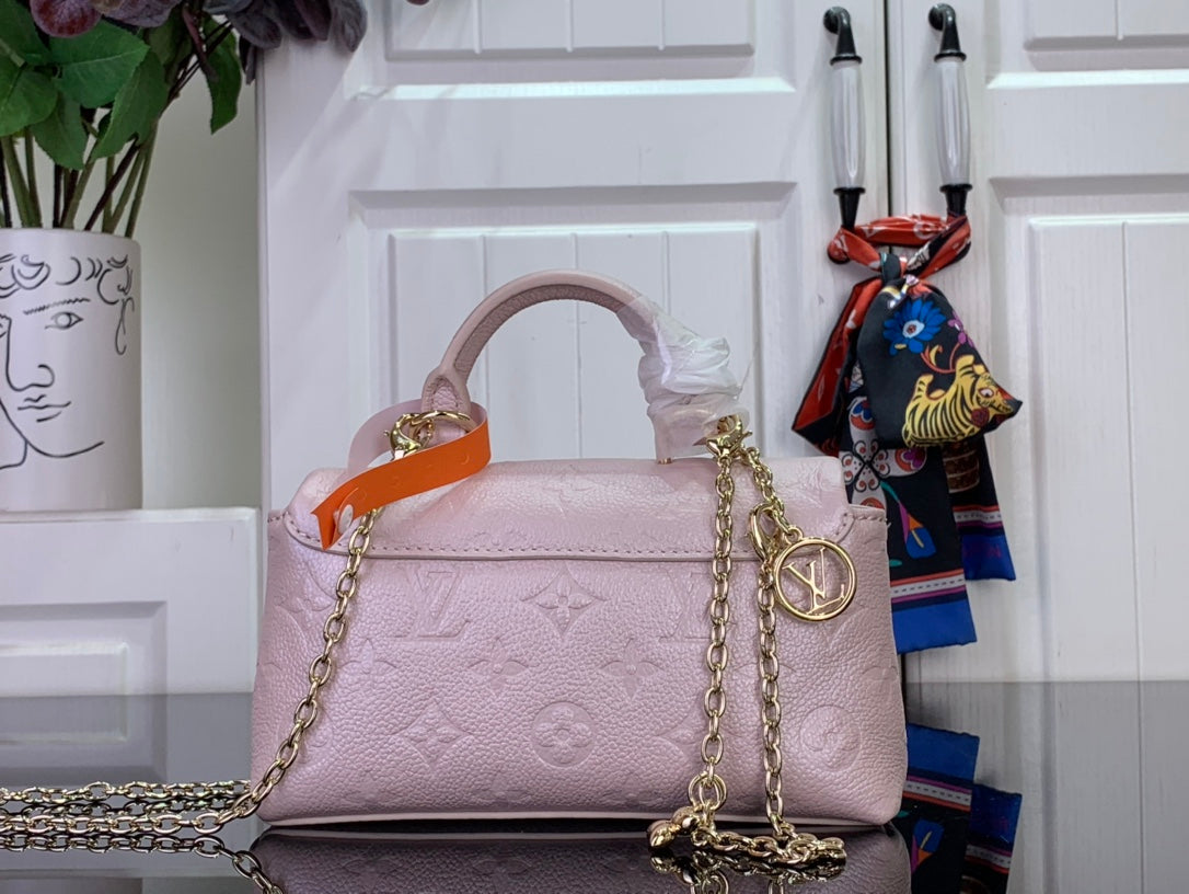 Light pink textured handbag with orange handle, gold chain strap, and gold ring detail.