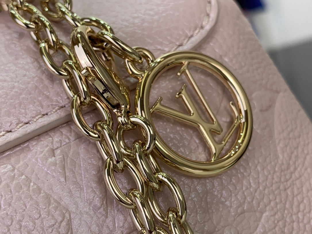 Gold chain and round clasp over light pink textured bag leather, close-up detail.