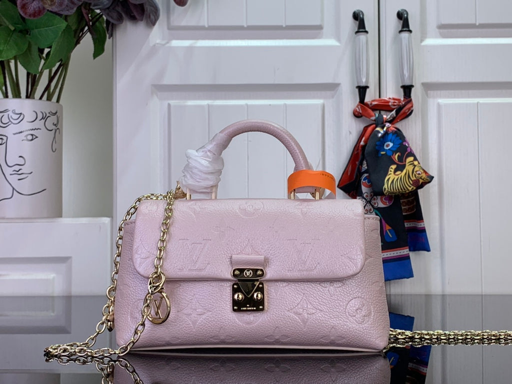 Light pink textured leather handbag with orange top handle, gold chain strap and front clasp.
